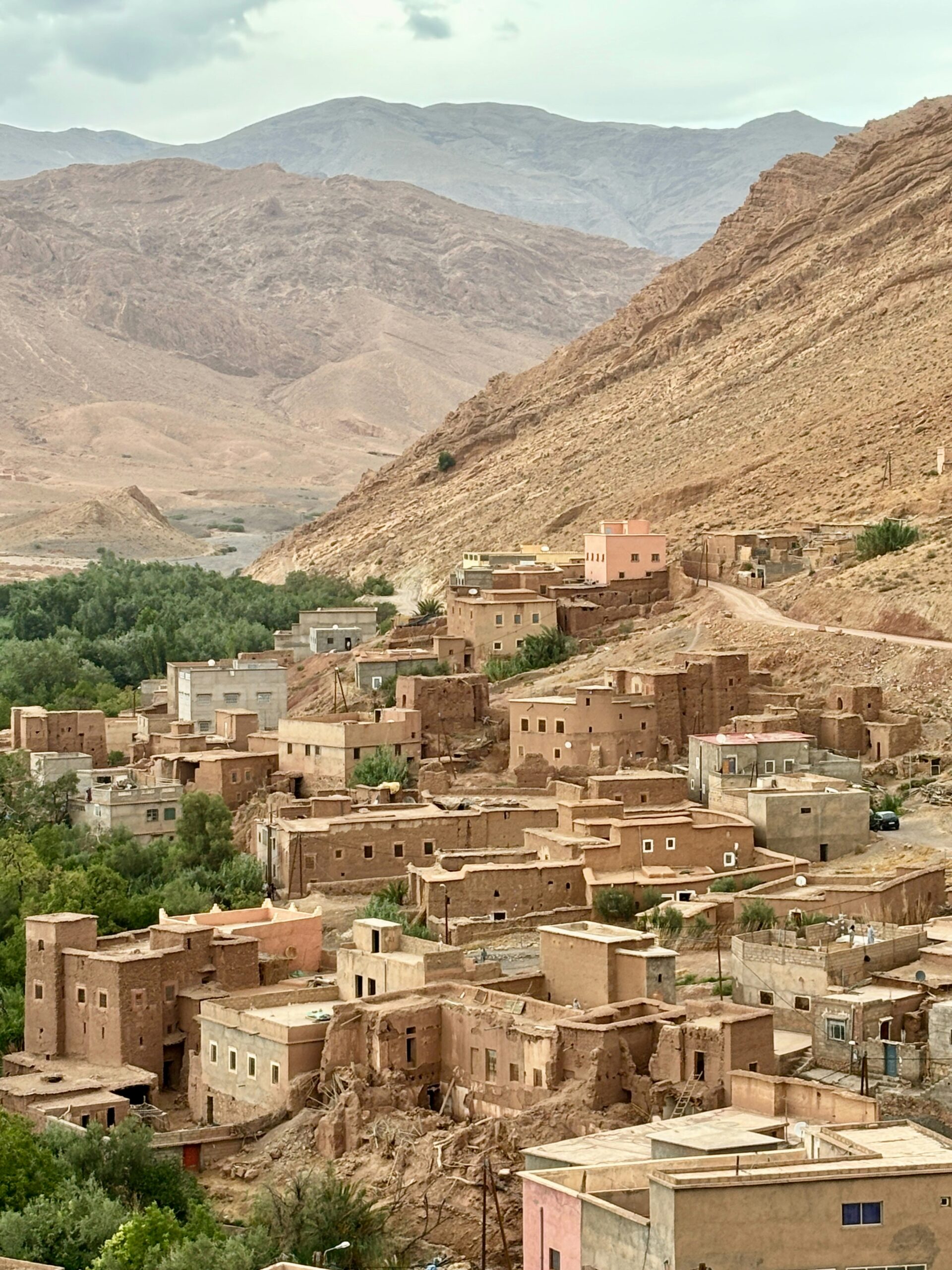 Earthen buildings in a village nestled against a steep rocky mountain slope